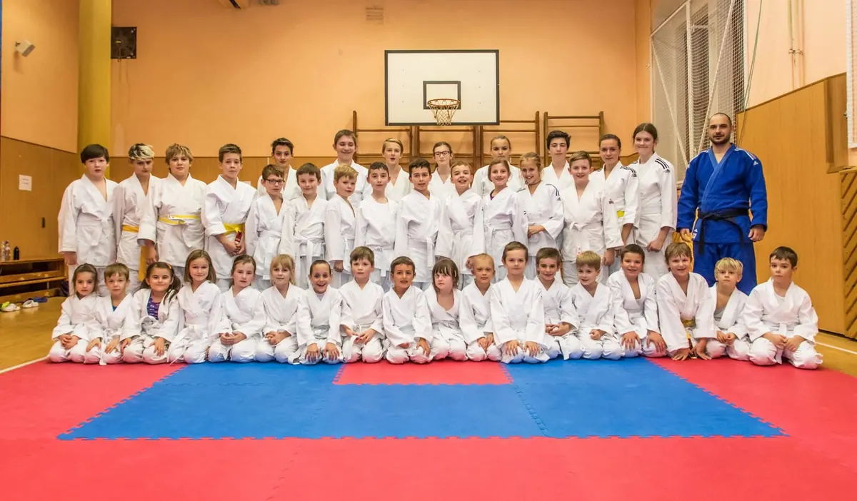 Skupinová fotka klubu RuKa JUDO — desítky dětí a trenér Karel v modrém judogi